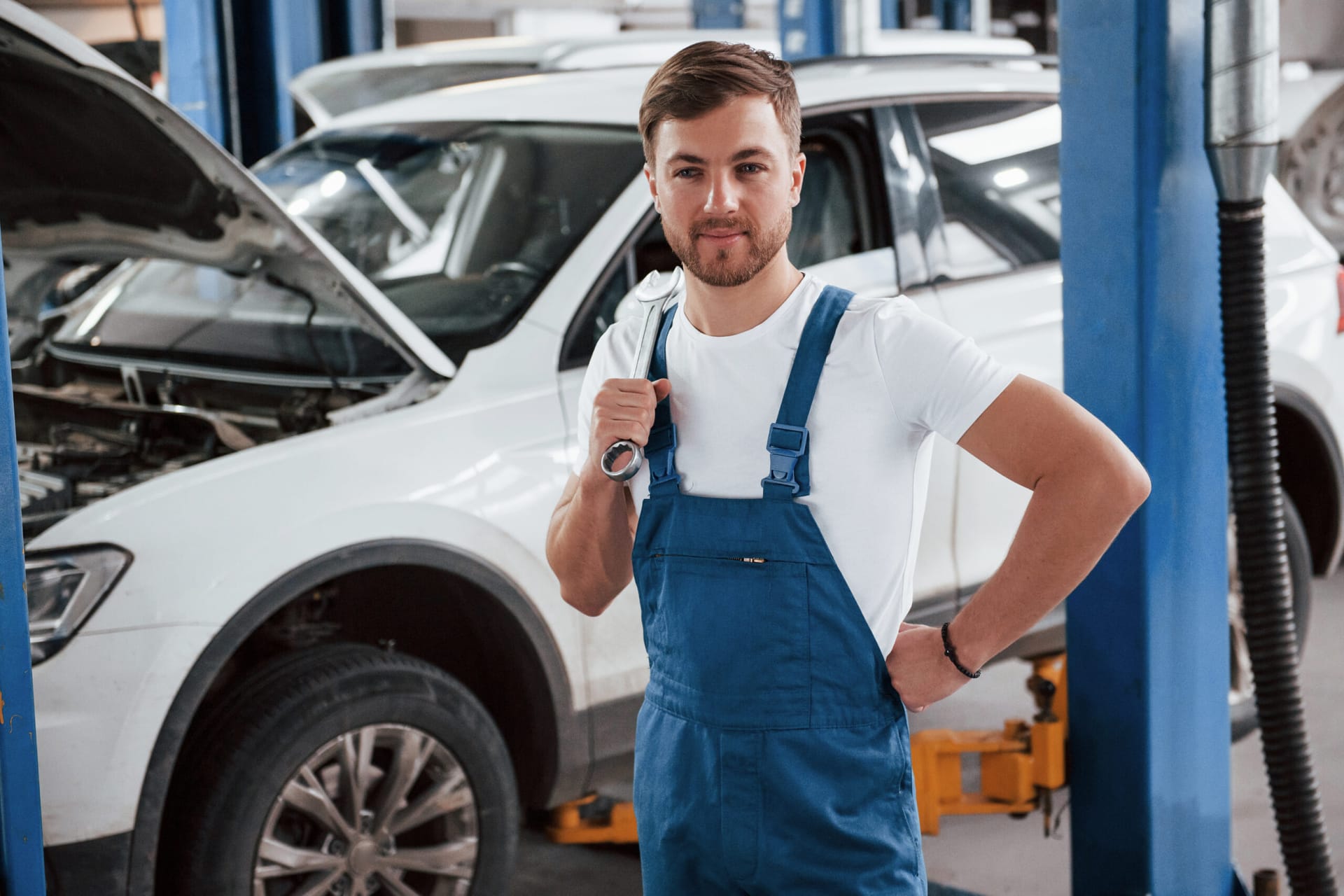 Standing with wrench in hand. Employee in the blue colored uniform works in the automobile salon.